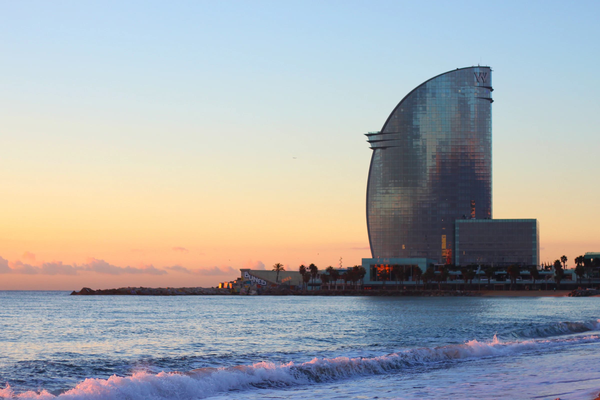 Waves and Barcelona’s sail-shaped waterfront building at sunset
